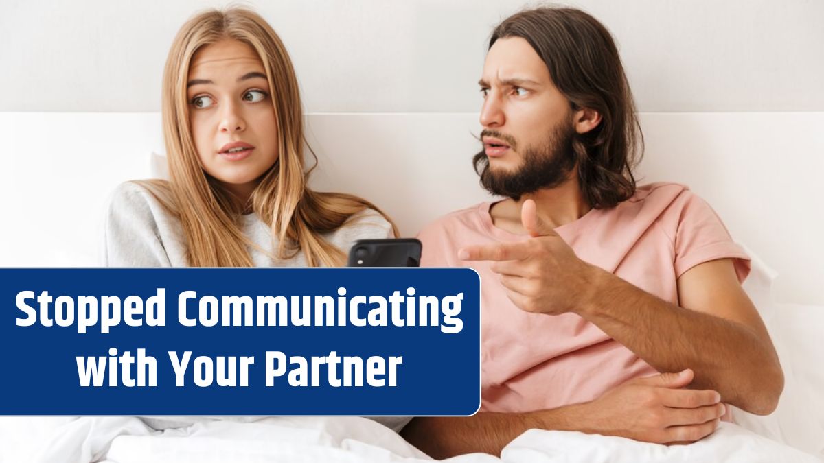 Beautiful confused young couple sitting in bed at home, pointing at mobile phone, having an argument.