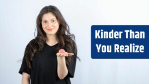 Young girl in black outfit holding pink cookie on white wall.